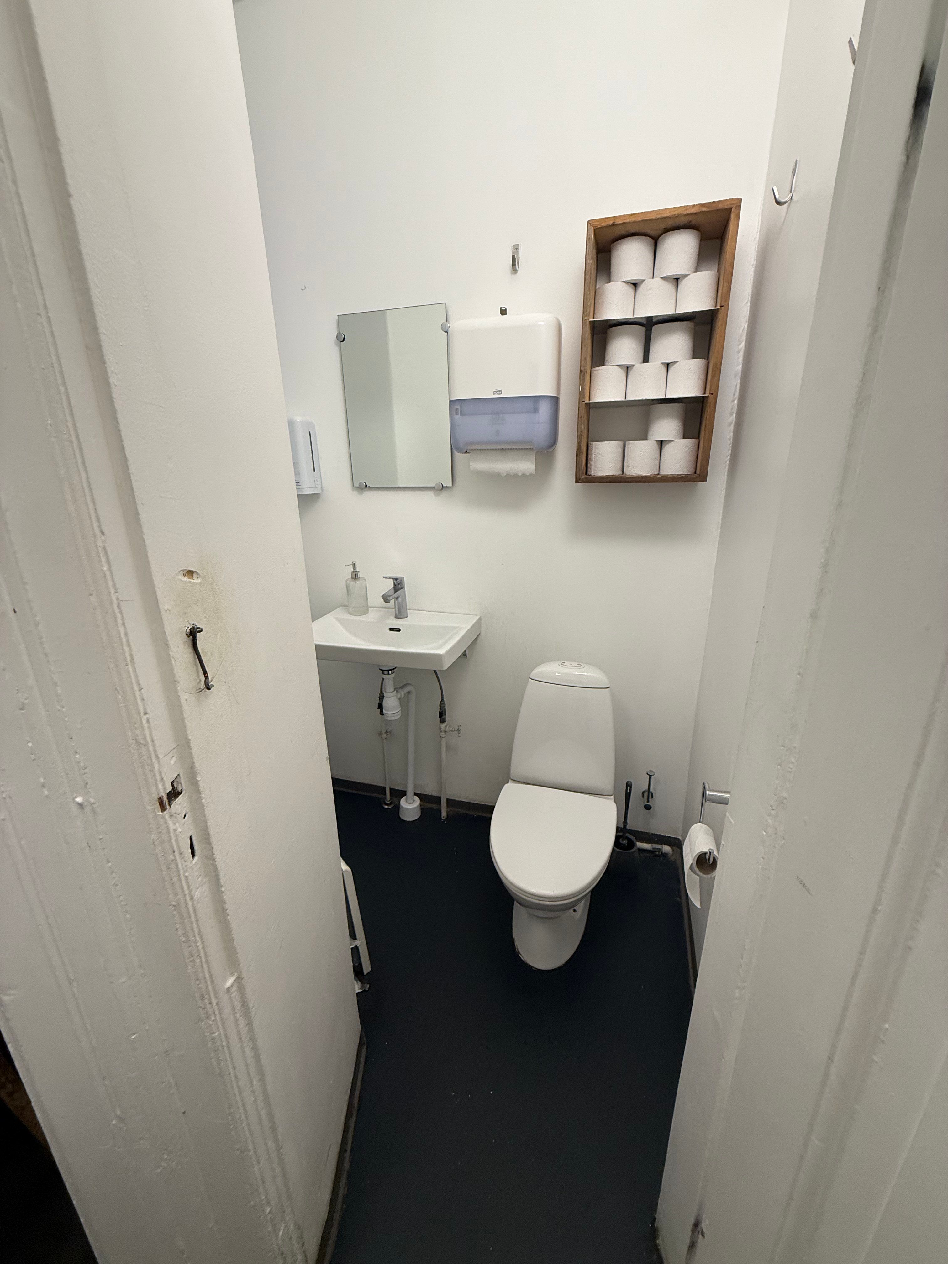 To moderne hvide toiletrum med toilet, håndvask, håndsæbe, håndklæder og toiletpapir.