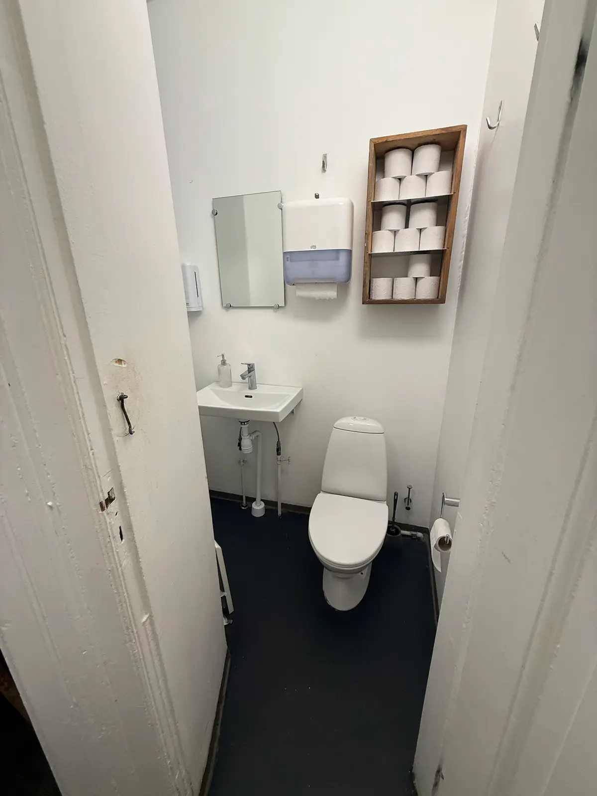 To moderne hvide toiletrum med toilet, håndvask, håndsæbe, håndklæder og toiletpapir.