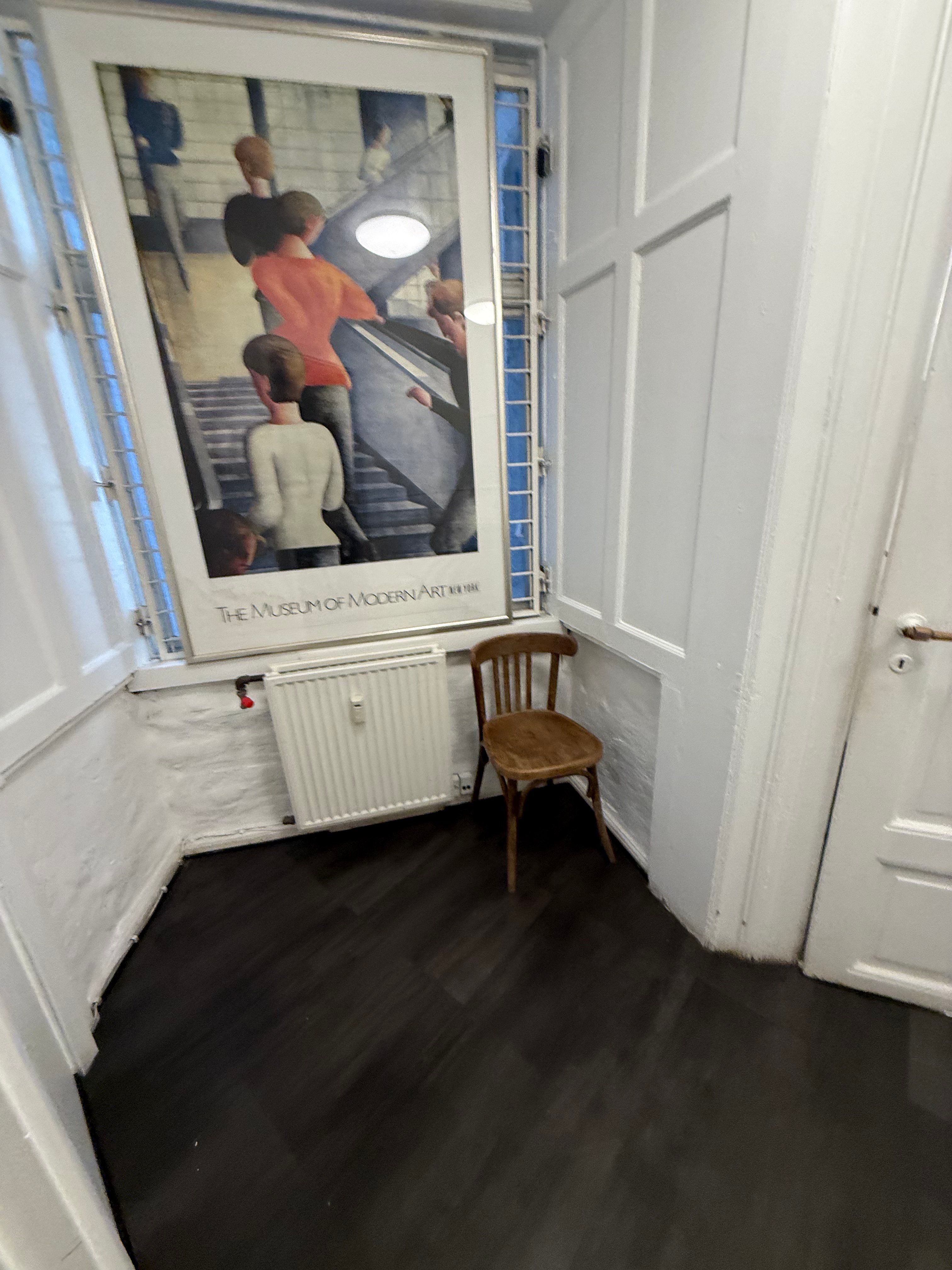 En lejlighed med et rum med et træstol og et radiator, som har en plakat på væggen