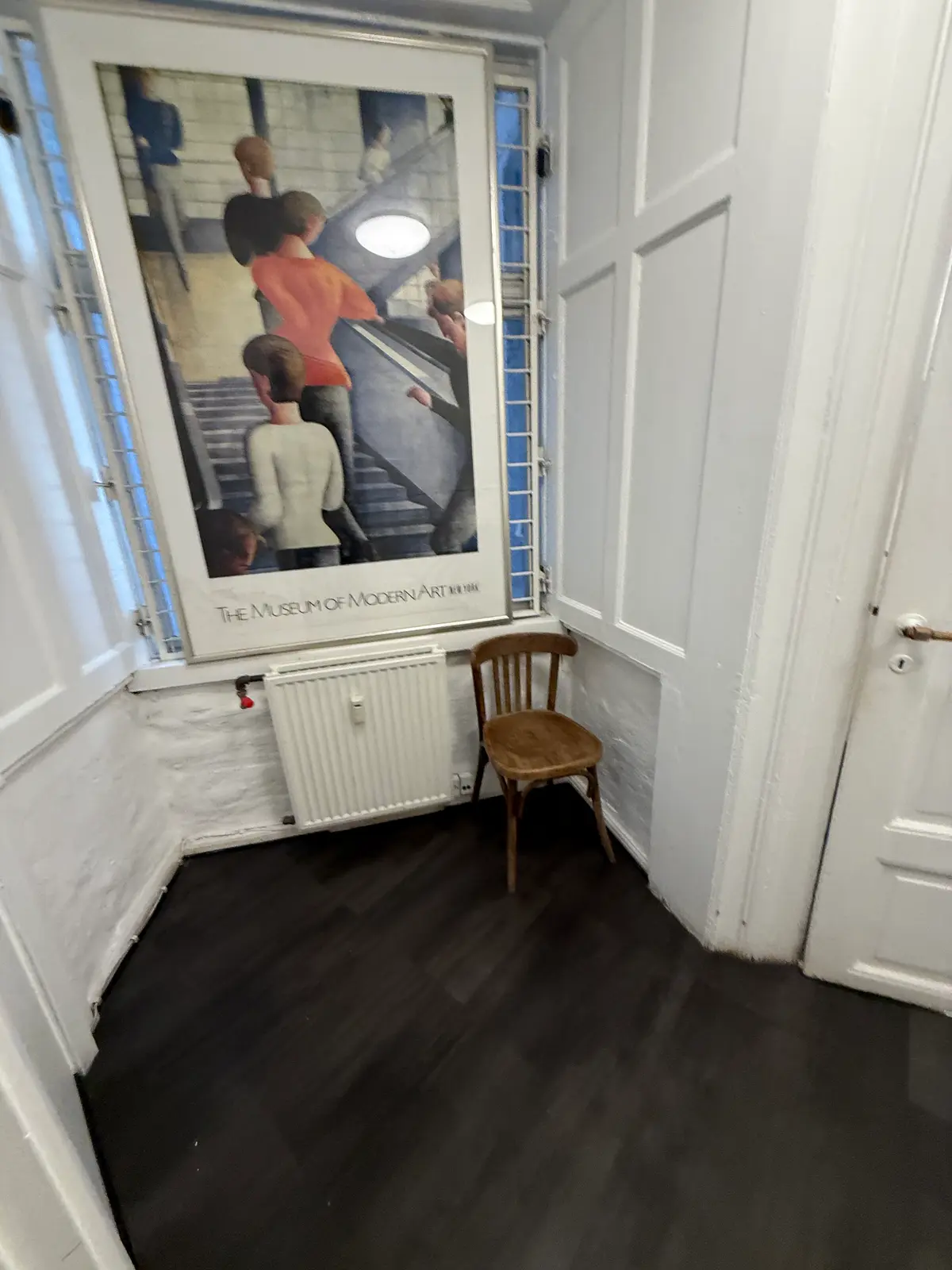 En lejlighed med et rum med et træstol og et radiator, som har en plakat på væggen