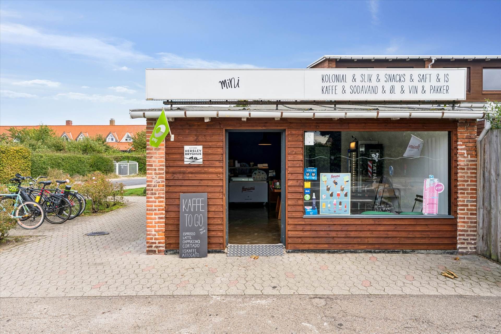 Kiosk med skilt, der læser "mini" og "Kaffe to go" samt flere cykler parkeret foran døren