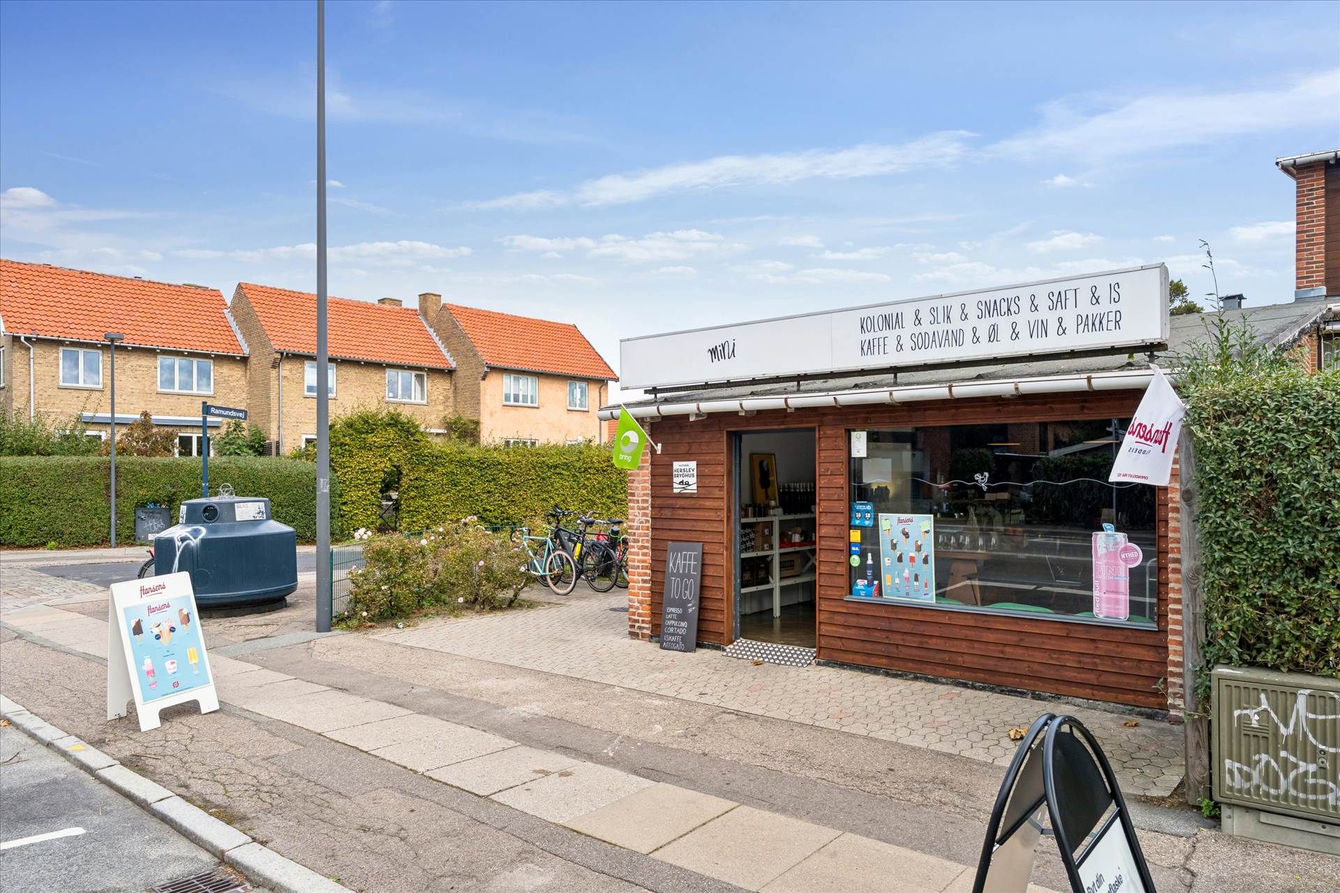 Kiosk med skrift, der læser Mini. Kiosken ligger på hjørnet af en gade og et boligområde. I butikken står der flere cykler