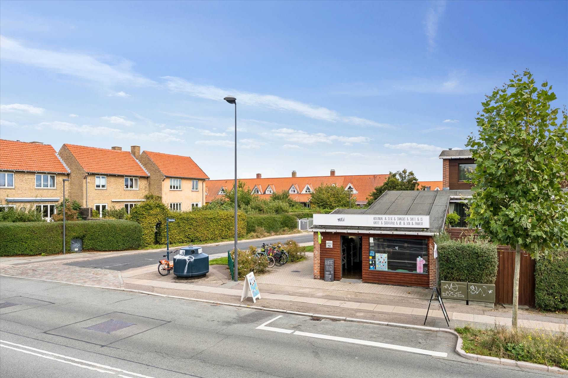 En butik med teksten "Kaffe og slik" og flere huse i baggrunden med orange tag og hvide ruder