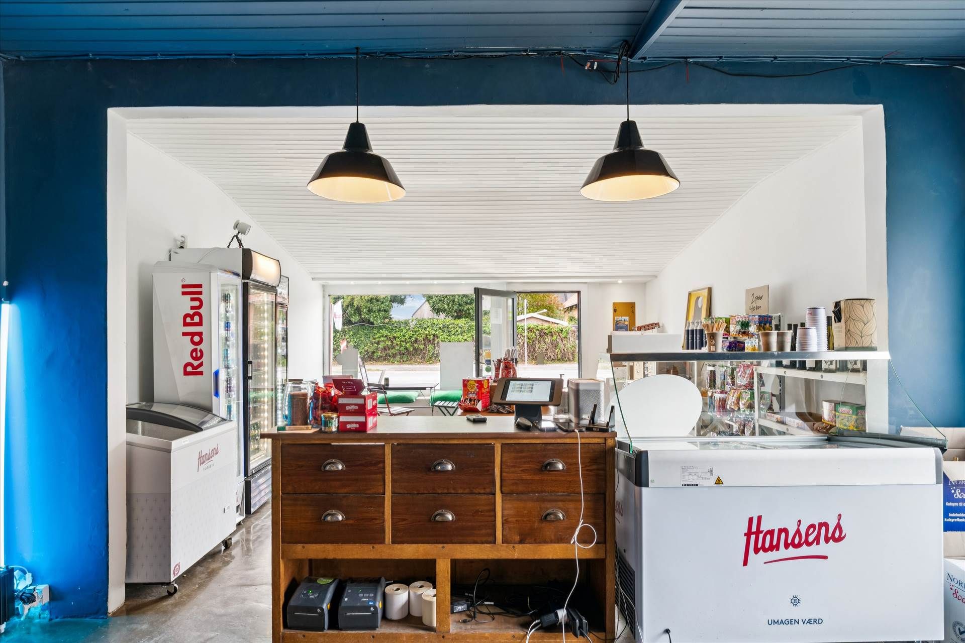 En kiosk med blå vægge og hvide lofter, med et skab med varer og et køleskab med Red Bull.