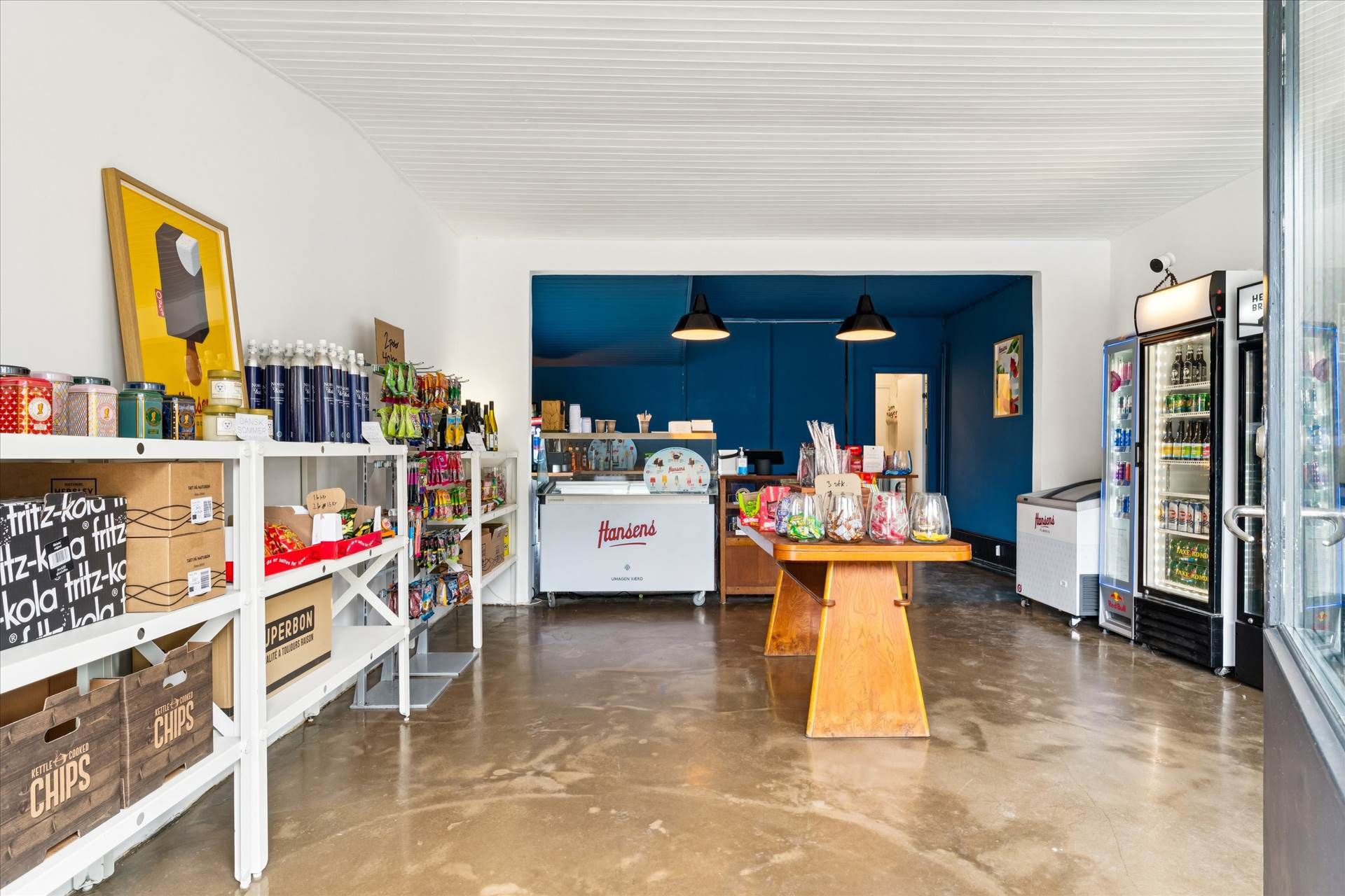 Kiosk med diverse produkter, is og drinks. Væg med skrift og bilderamme samt køleskabe med sodavand og energidrikke.