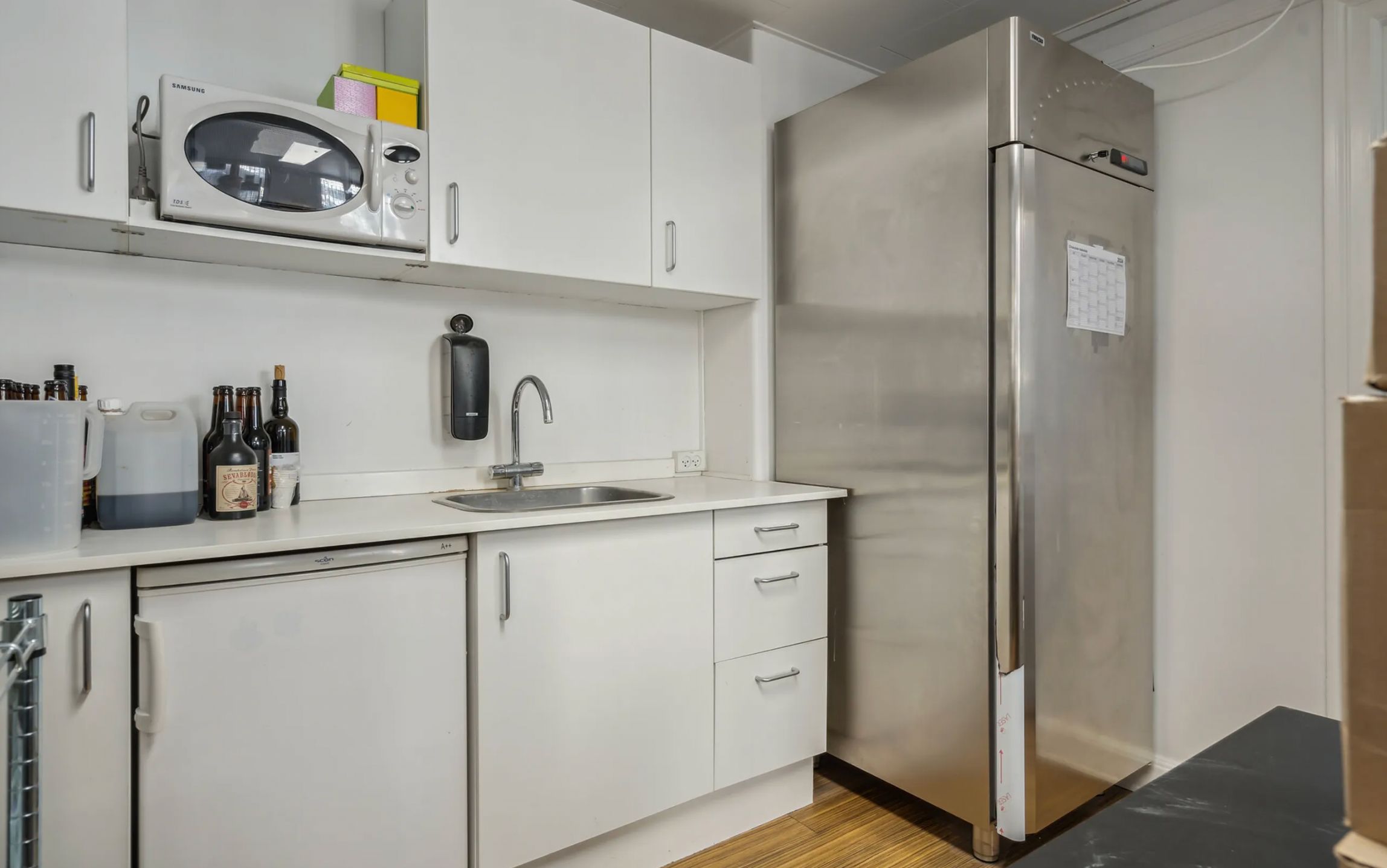 Moderne køkken med hvidt skab, stålkøleskab og komfur, indretning med mikrobølgeovn, stålvaskedispenser og glasflasker