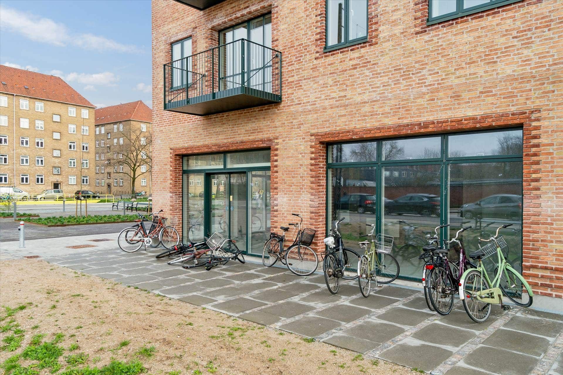 Både nye og brugte cykler er parkeret foran et hus med glasruder og balkon