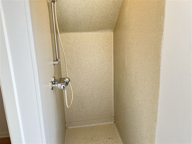 En lille badeværelse med åben dør og hånddusch i loftet med slange og håndtag