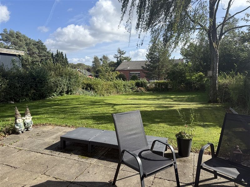 To stole med læne samt en sollygter i dagslys på terrasse med udsigt over grønne enge, hvor en plante i potte står