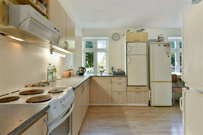 Køkken med to køleskabe, ovn, grydeklud, kaffemaskine, flasker og tallerkener på en hvid trægulv