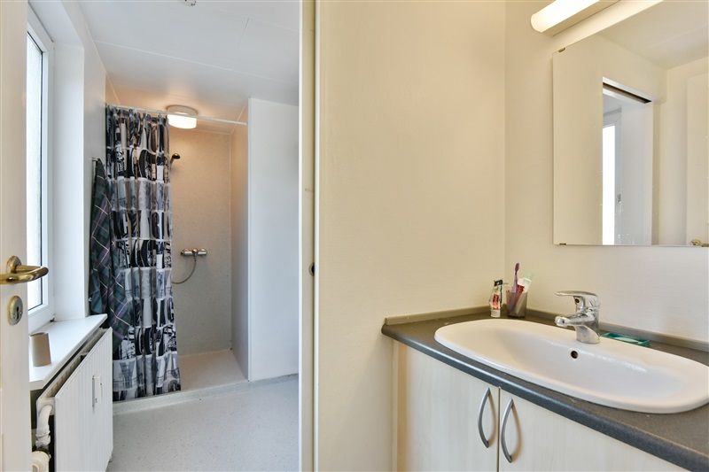 Velholdt badeværelse med hvidt skab, lysekron, hvidt vasketøjsskab og håndklædekurv. På væggen er der et spejl og en