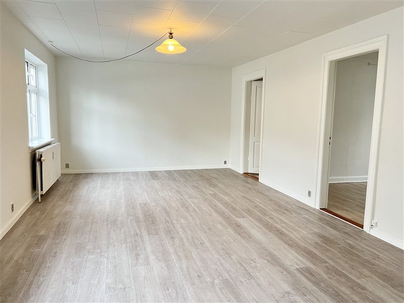 En tom lejlighed med hvide vægge og gulv og et enkelt gult lampeskift i loftet