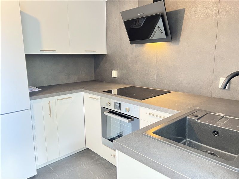 Moderne køkken med hvide skabe, sort induktionskomfur, indbygget ovn, gråt arbejdsbord og lysegrå væg med lysegrå gulvfliser