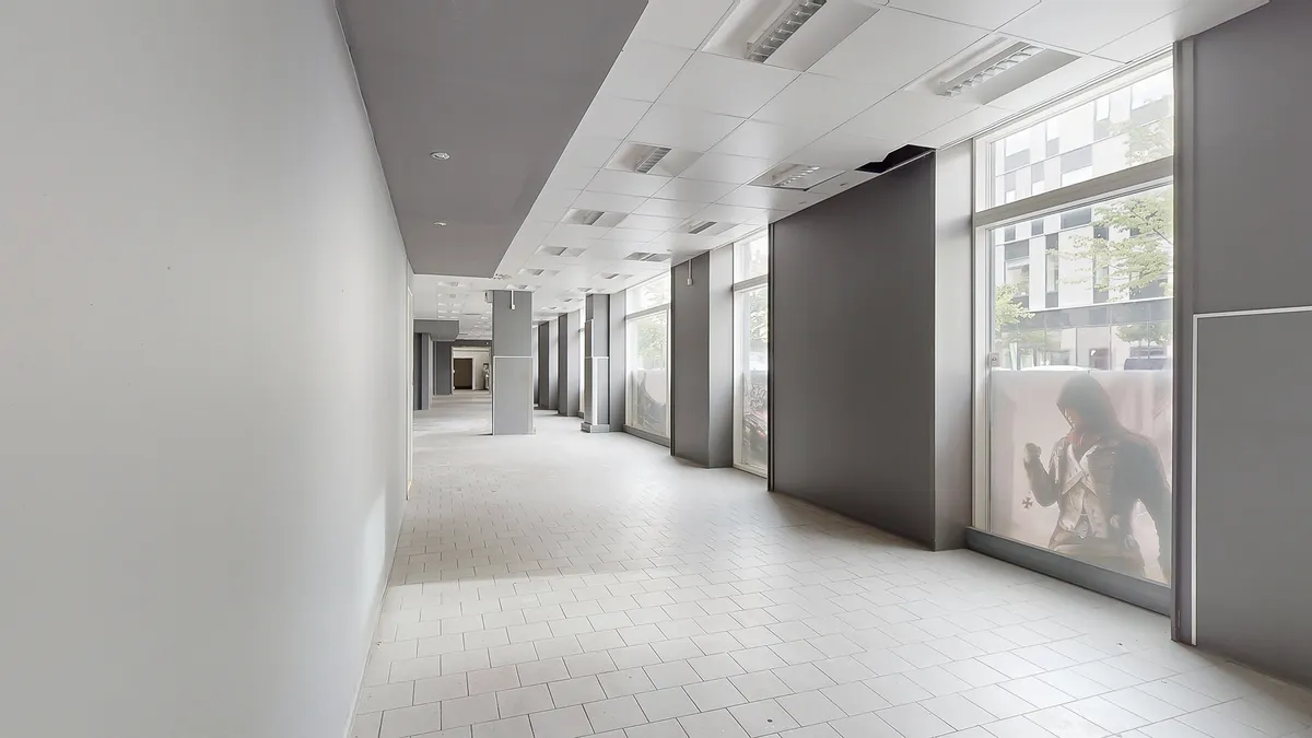 Kort og tæt forretningscenter med hvidt loft, hvide vægge og hvide gulvfliser samt glasvinduer og stående reklameskilte