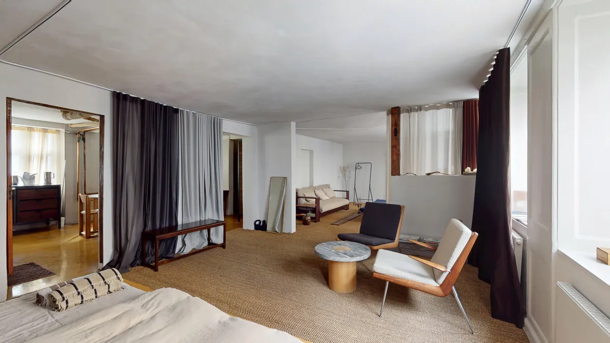 Et elegant, moderne værelse med hvid og brun farvetone, massivt træ, komfortable møbler og lyse gardiner. Der er et trægulv