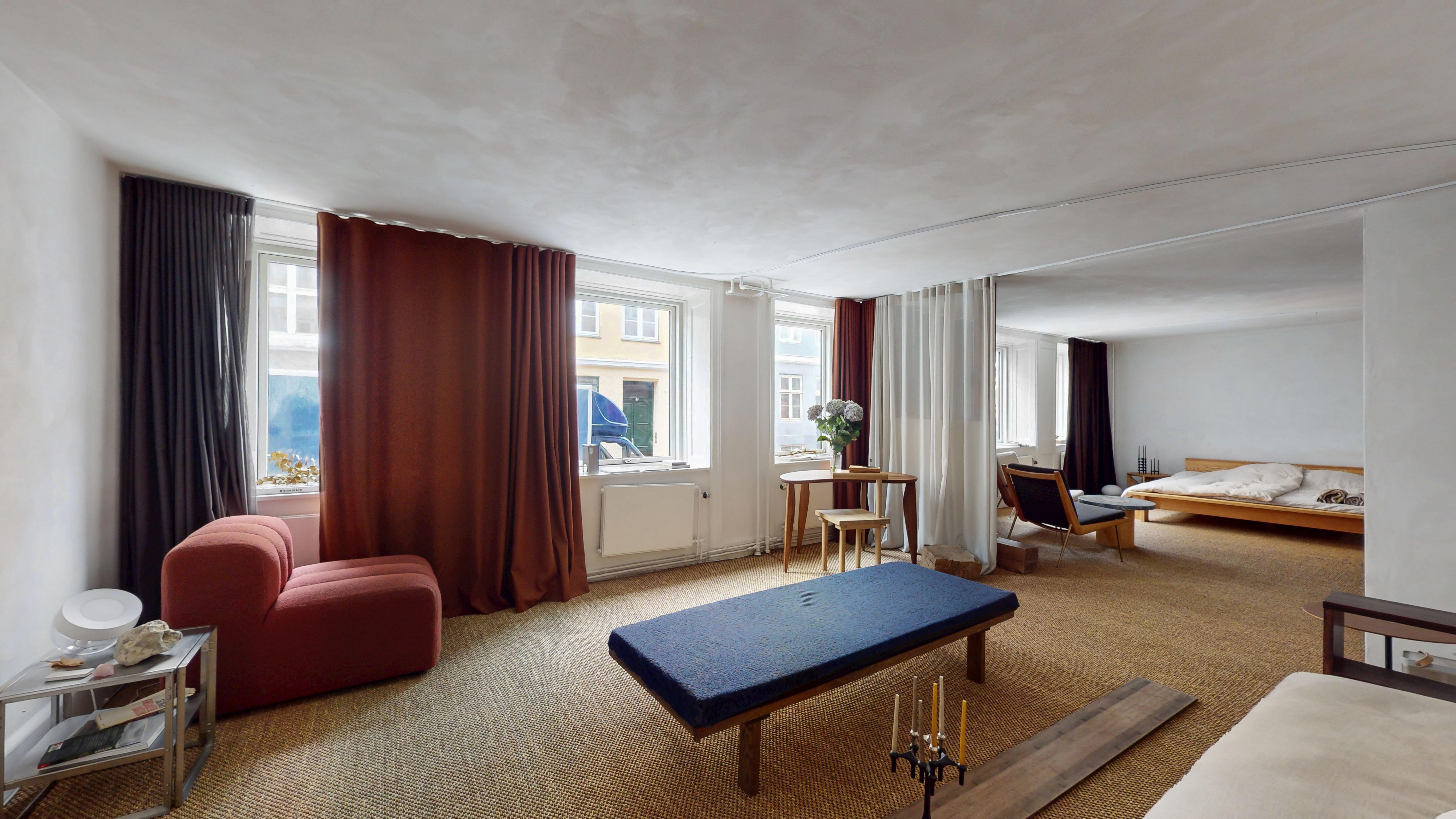 Minimalistisk stue med lyse farver og en sofa med høje læne, et bord med blomster og en stol, samt et soveværelse med en