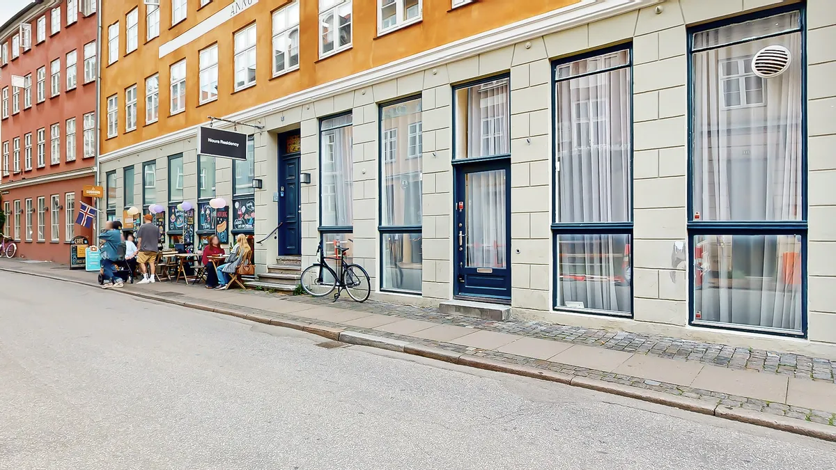 En gruppe mennesker sidder på en terrasse foran en butik, der er indrettet i en rødere og kreativ stil