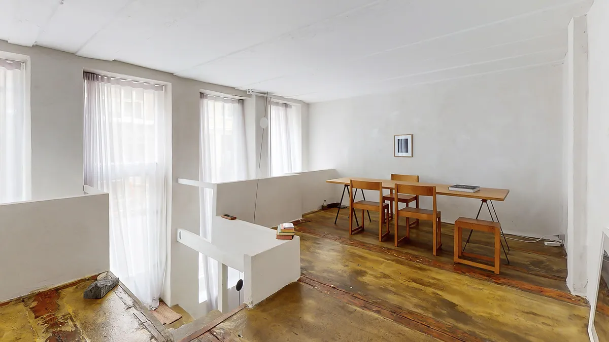 Rå og kreativt indrettet rum med lyse vinduerne og højloftede lofter, der giver en åben og inspirerende atmosfære.