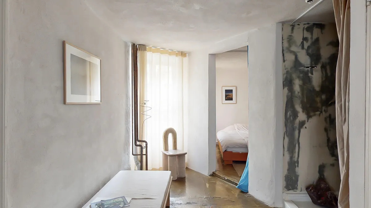 Råt hvidt loft og vægge i en minimalistisk rumindretning med en hvid stol og en sofa i et soveværelse med en skandinavisk