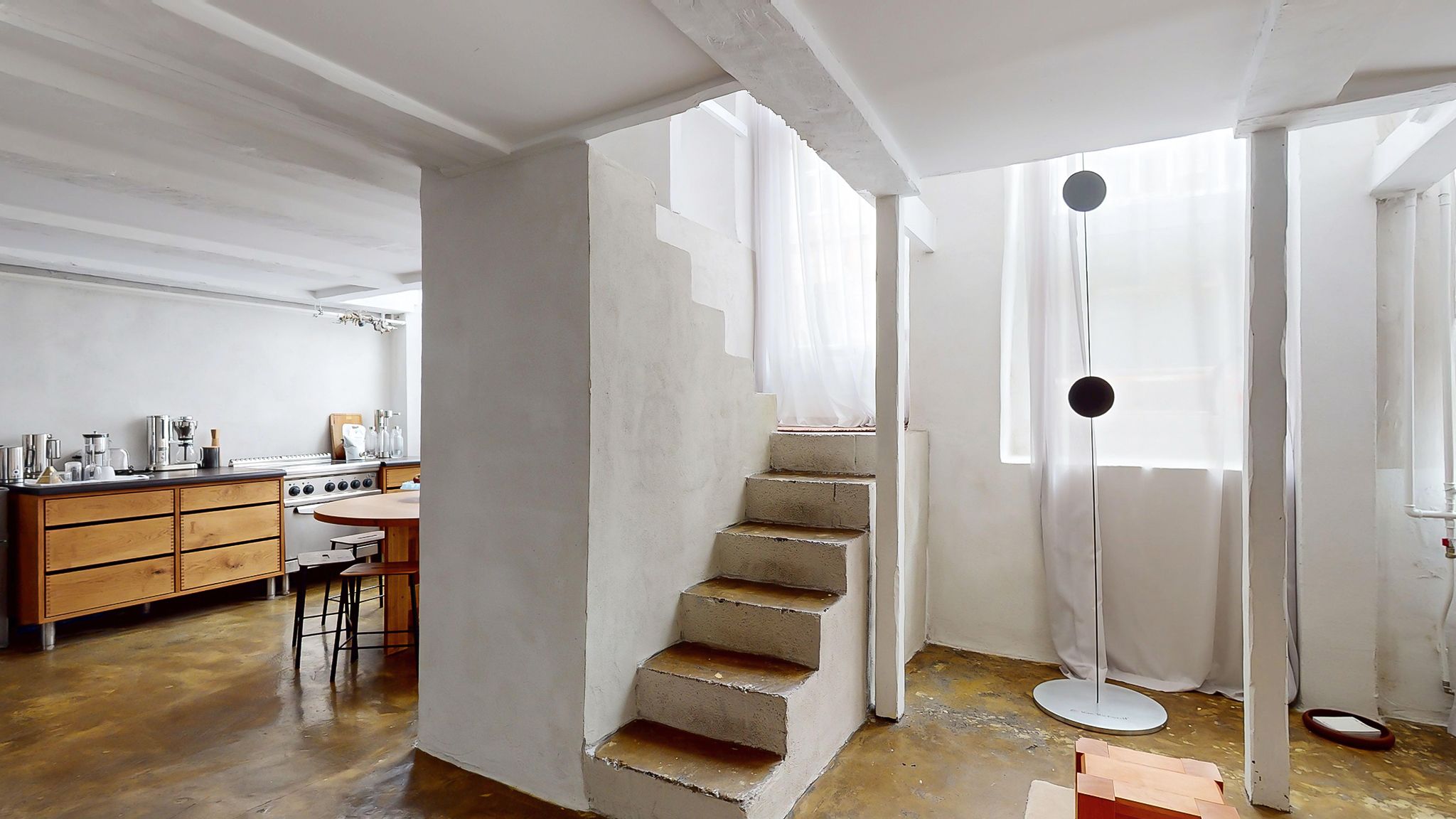 Et moderne interiør med rå beton og lysefarvede vægge, høje lofter og lysegardiner, der danner en åben og inspirerende