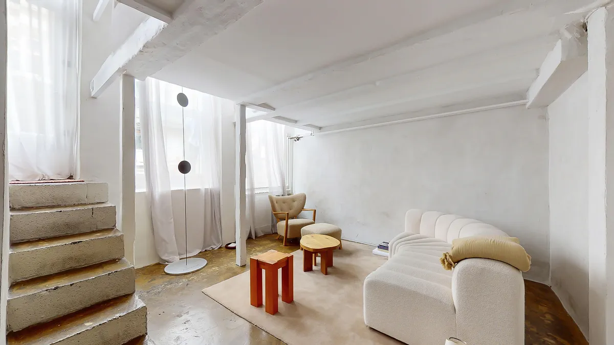 Moderne og minimalistisk værelse med hvid væg og trægulv, sofa, bord og stol, samt loft med hvide bælge og loftsvinduer med