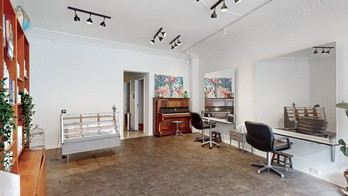 Salon med stol, piano, vægmalerier, spejl og plante. Køkken med skabselementer og plante. Lampearmaturer og vægdekorationer