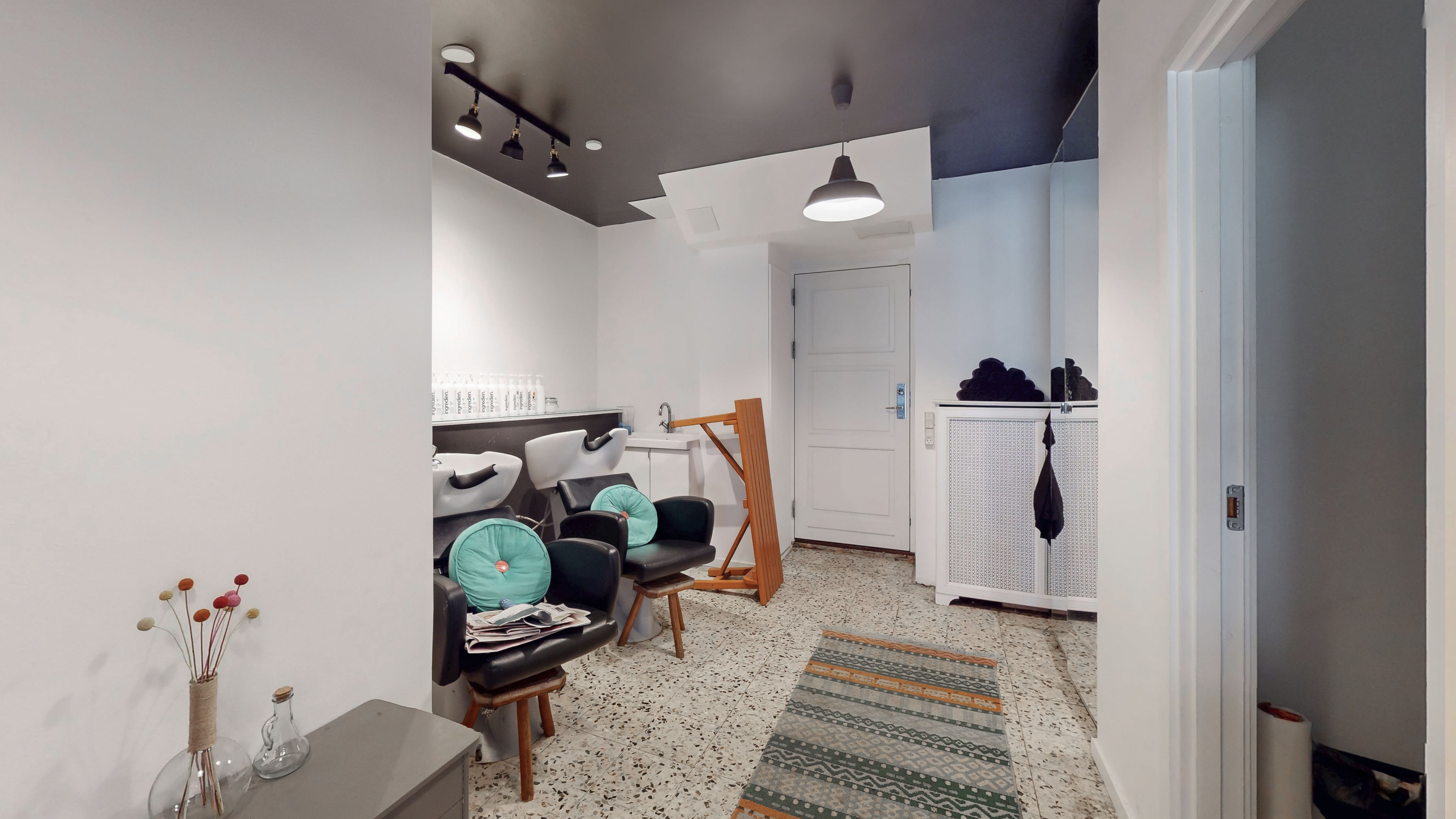 En moderne og veludstyret frisørsalon med hvide vægge, lysekroner, lyse hårstole, et skab og en gulvtæppe