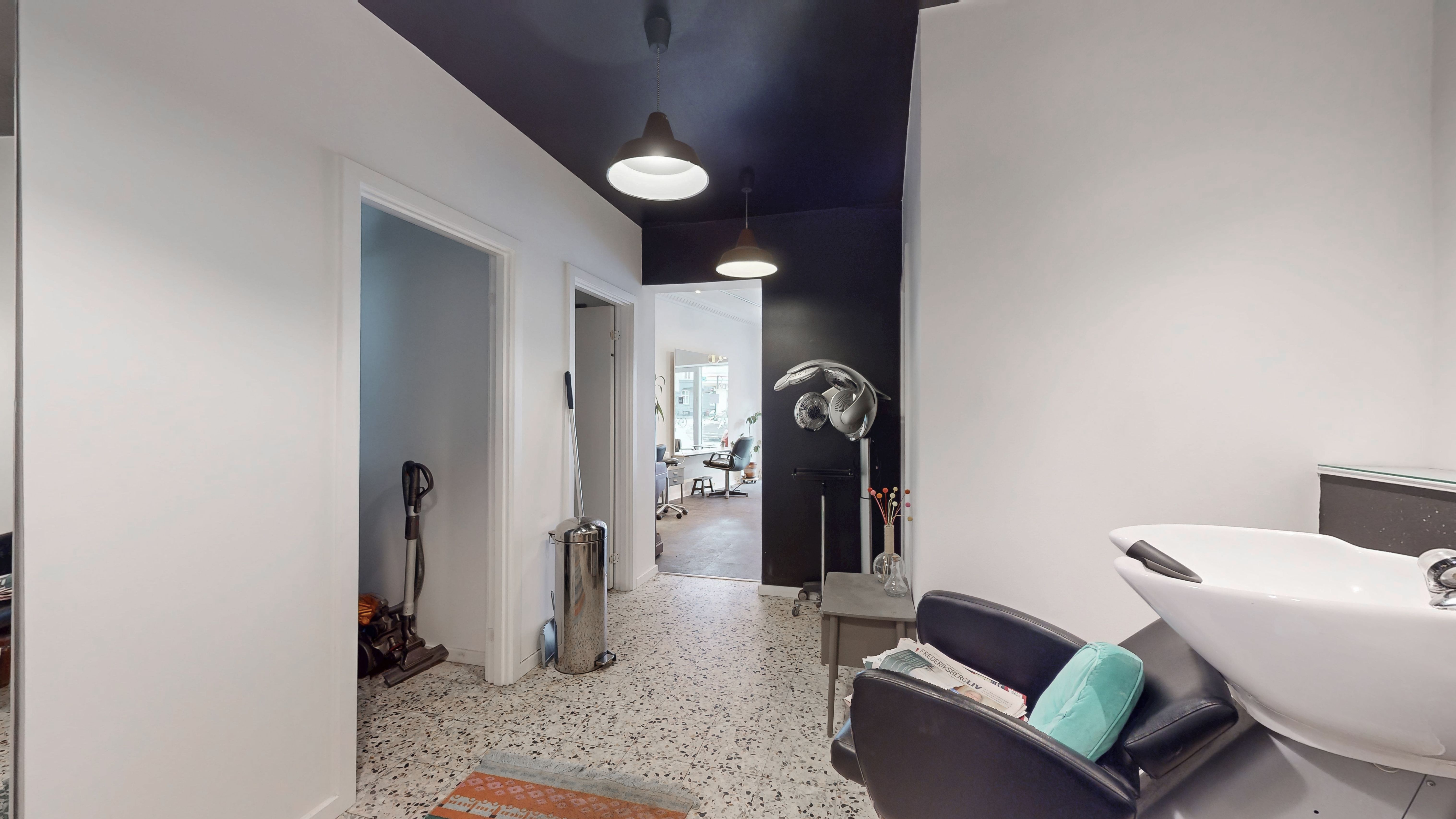 En moderne og pæn frisørsalon med hvid gulvbelægning og mørke lofter samt en stor hvid vaskeskål og en lænestol med pude