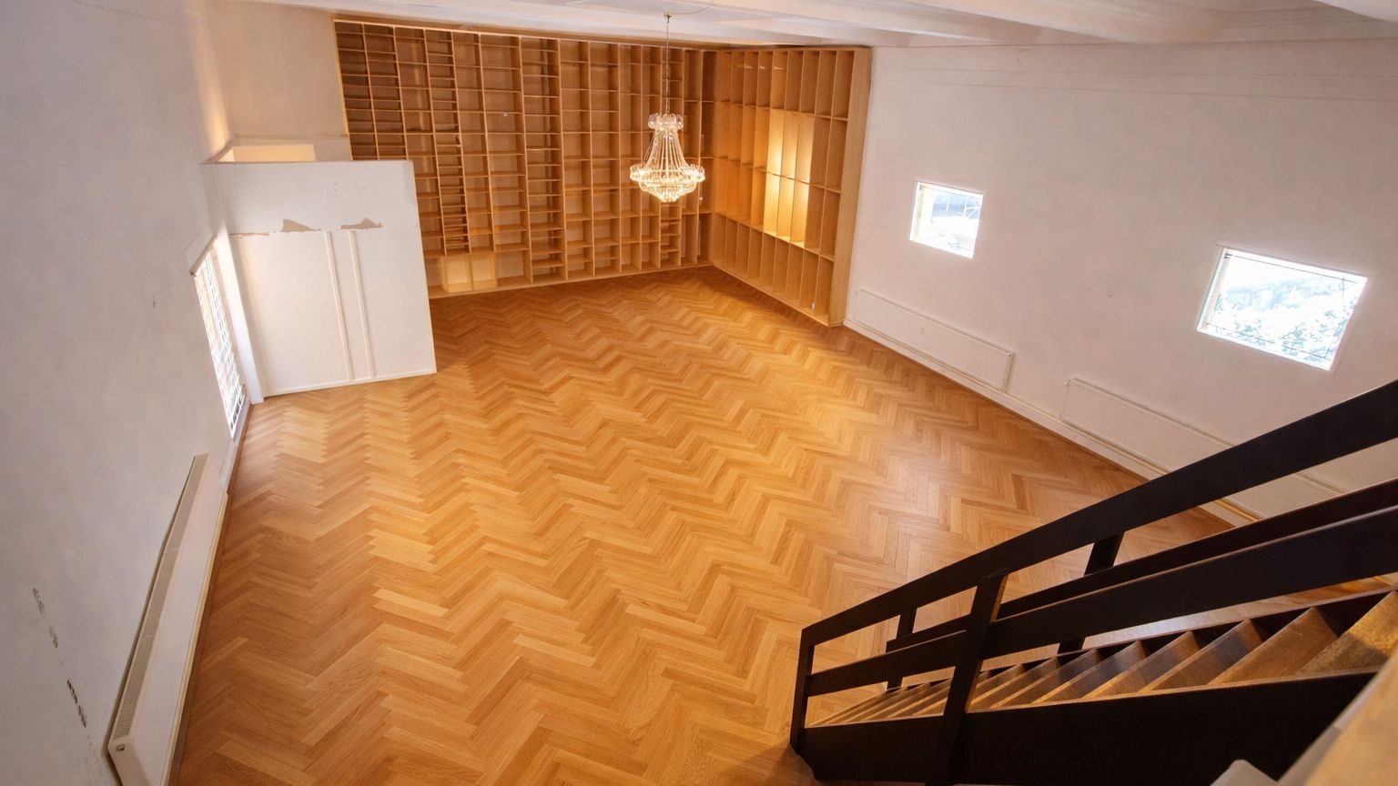 Et stort og åbent lokale med trægulv og højt loft, der giver plads til et stort bibliotek og en indgangsdør til højre.