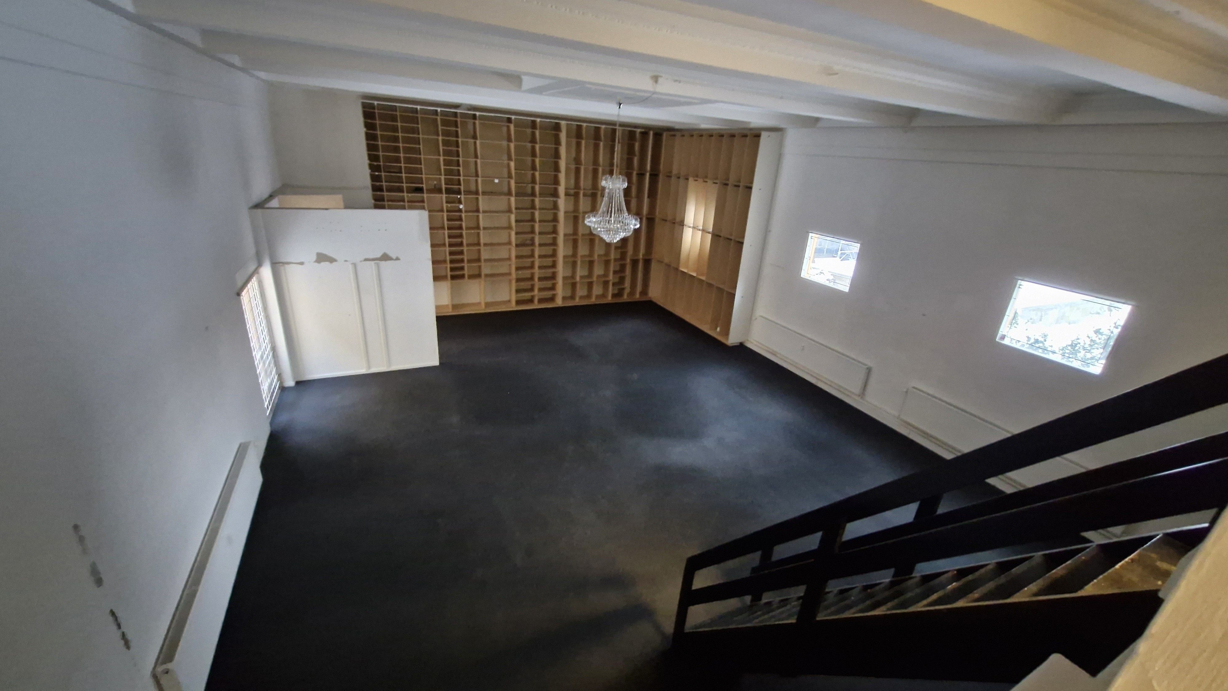 Forladt og moderne lokale med lyse lofter, lysekroner og tre vinduer med udsigt til gaden