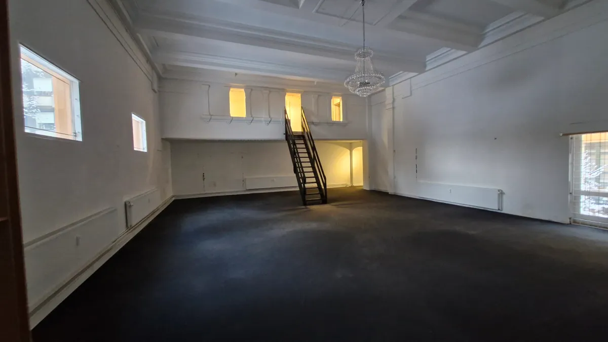 Et stort tomt lokale med højt loft og en stor lysekron, stige og flere vinduer med udgang til en gang