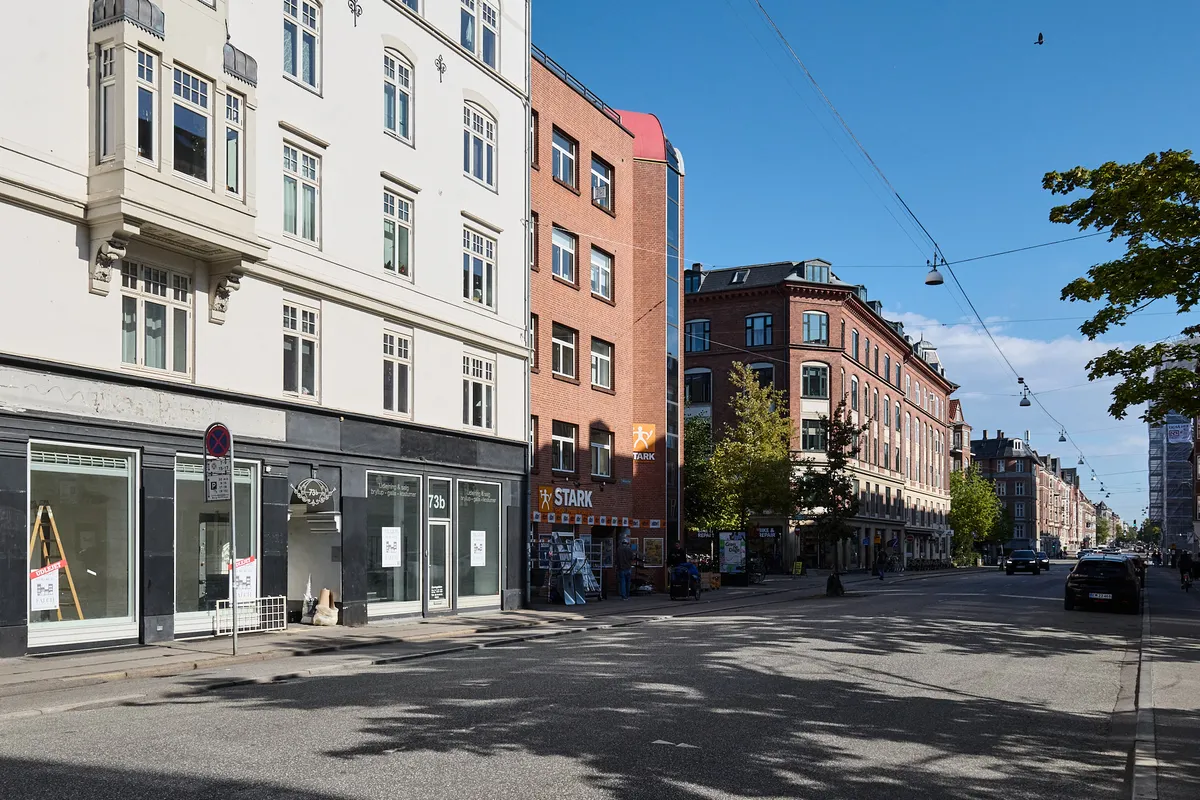 En butik med reklameskilte står på Falkoner Allé med træer og kørende biler i baggrunden