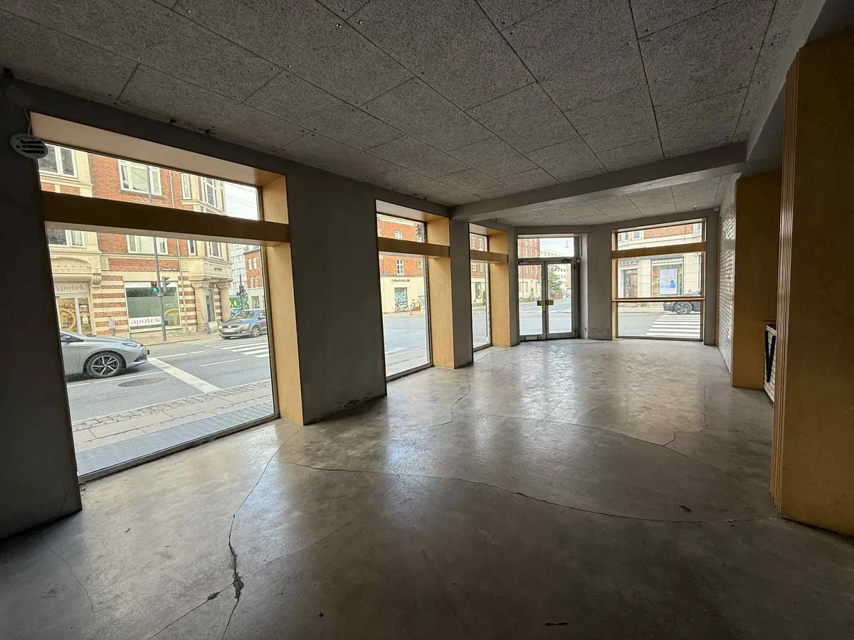 Forretningslokaler med 3 vinduer, hvorfra der er udsigt til en gågade med biler og et kryds