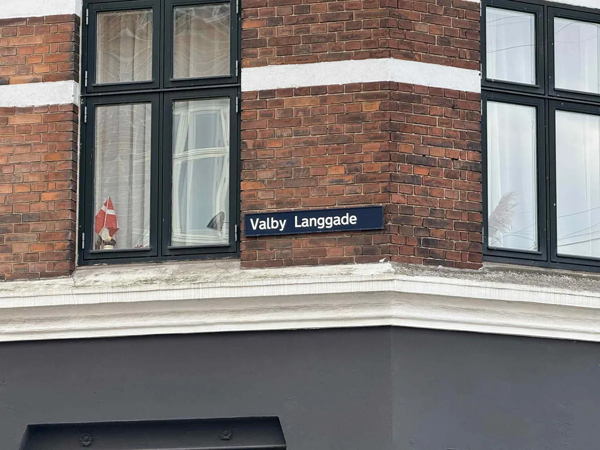 En teglbygning med vinduesglas og et navneskilt på Valby Langgade, der tyder på en bygningsadresse.