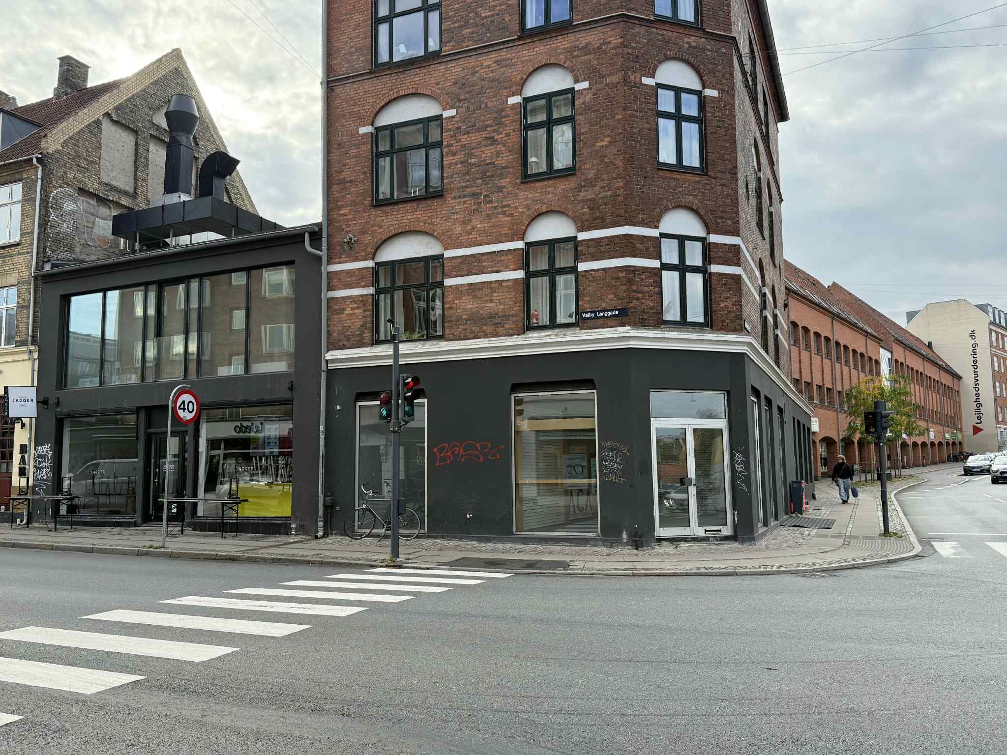 Hjørnebygning med skrift og graffiti, rødt murværk og gult vægmaleri, stribet fortov og gågade