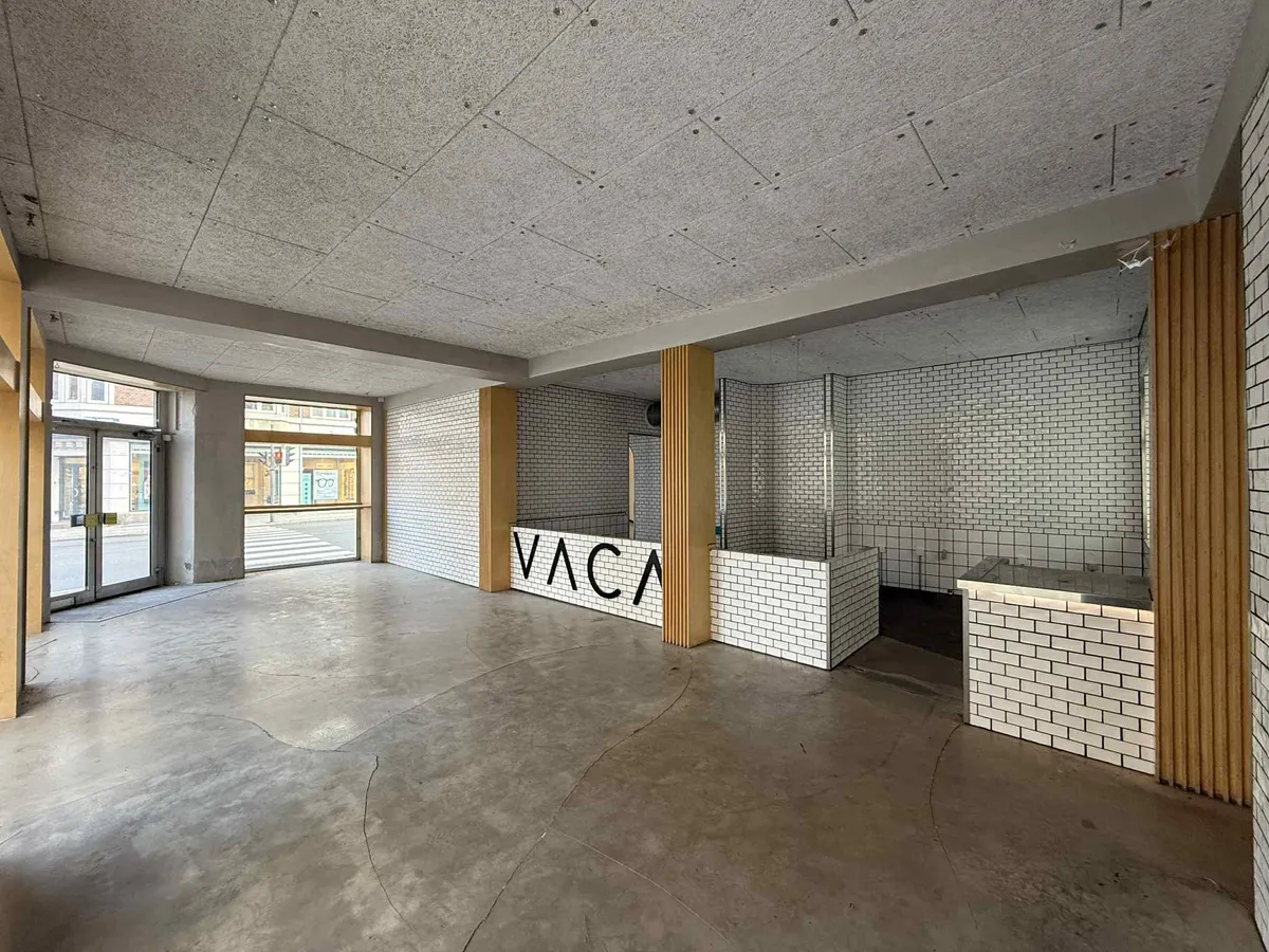 Tom lokale med glasdøre og vinduer, højt loft, hvidt tøj, møbler og teksturer, og "VACA"-logo på væggen