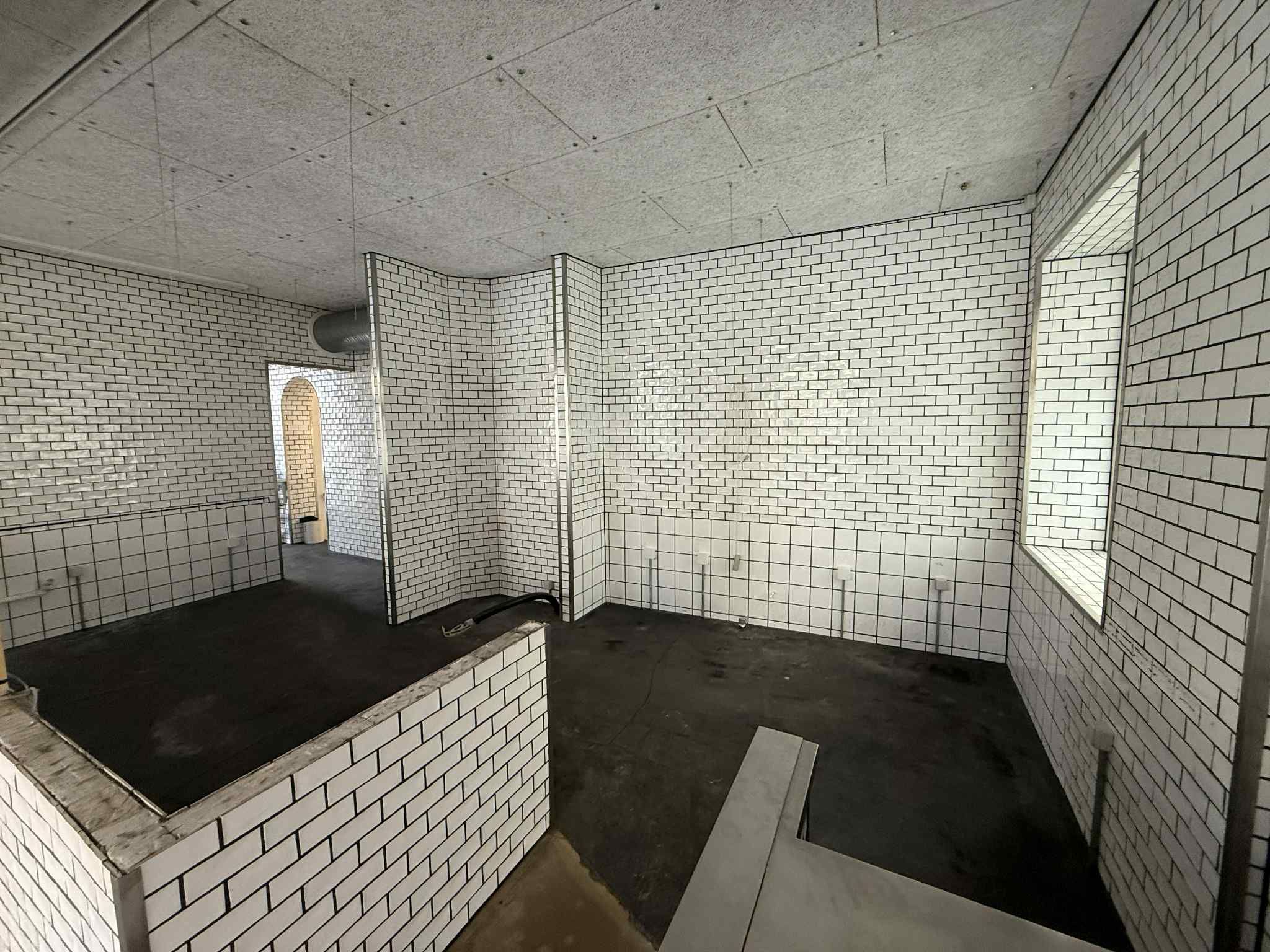 Et rum med hvide mursten og sort gulv samt et rektangulært hul på væggen og et vindue