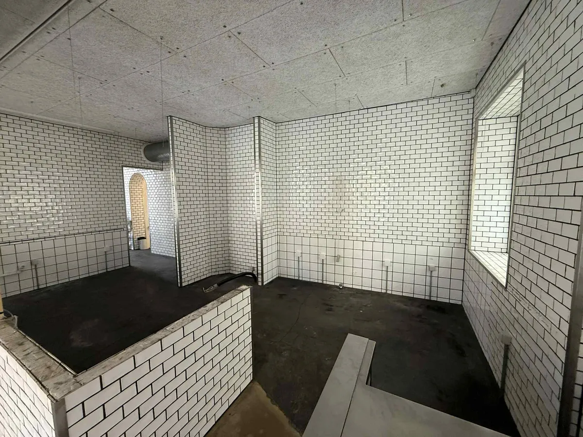 Et rum med hvide mursten og sort gulv samt et rektangulært hul på væggen og et vindue