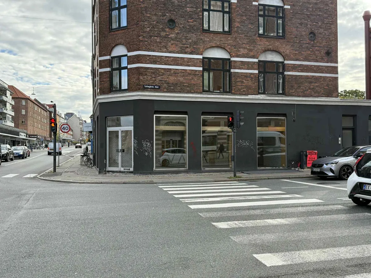 Forretningsbygning med glasvinduer og graffiti på væggen og en vej med biler og cykler på en hjørnegrund.