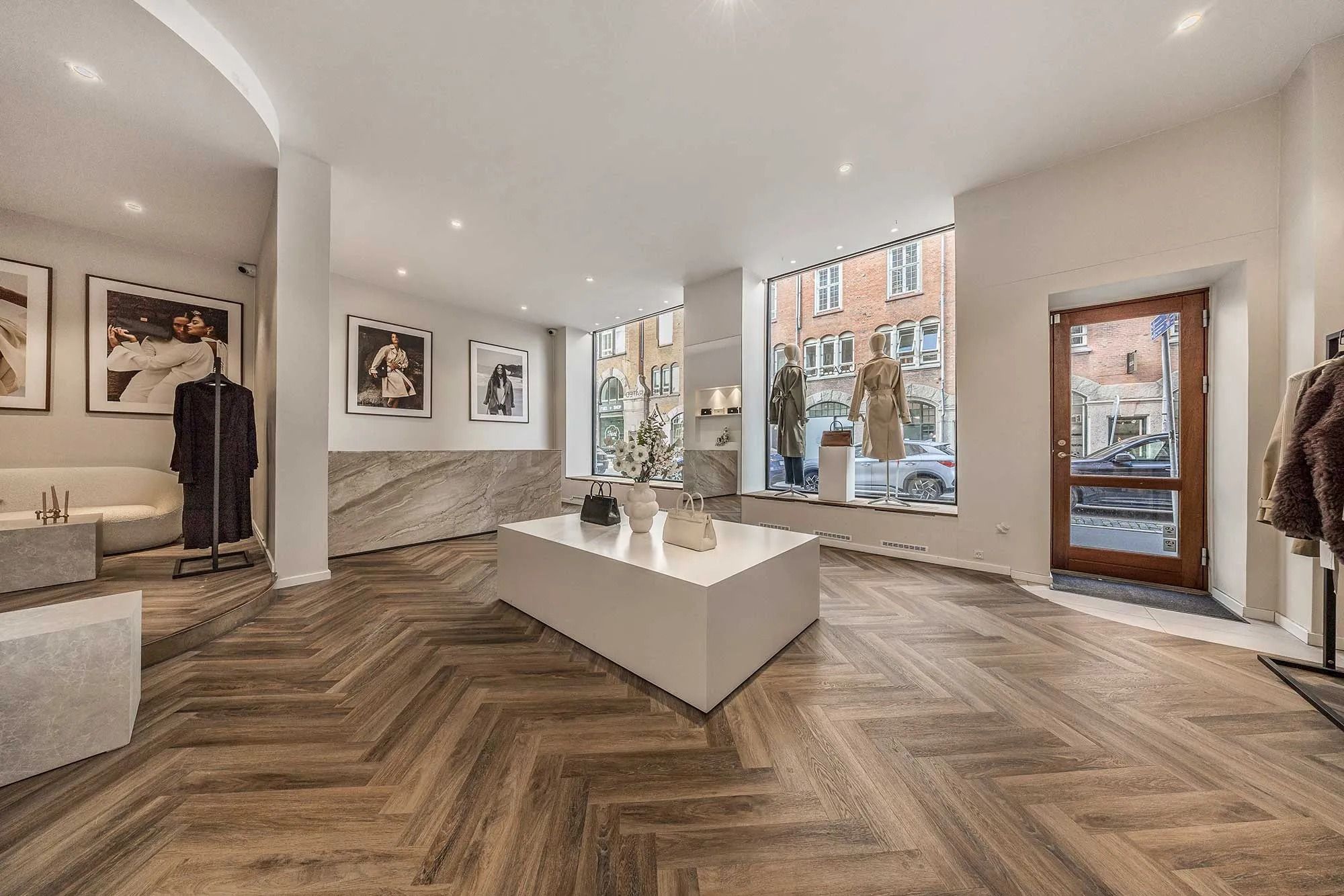 Flot og højloftet butikslejemål med lyse lofter, trægulv og hvide vægge. I butikken er der et stort skrivebord og flere lyse