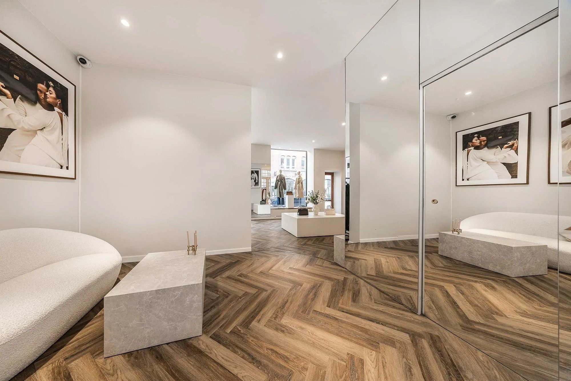 Flot og højloftet butikslejemål med elegant interiør, hvid vægdekoration og trægulv samt smukke møbler og spejl