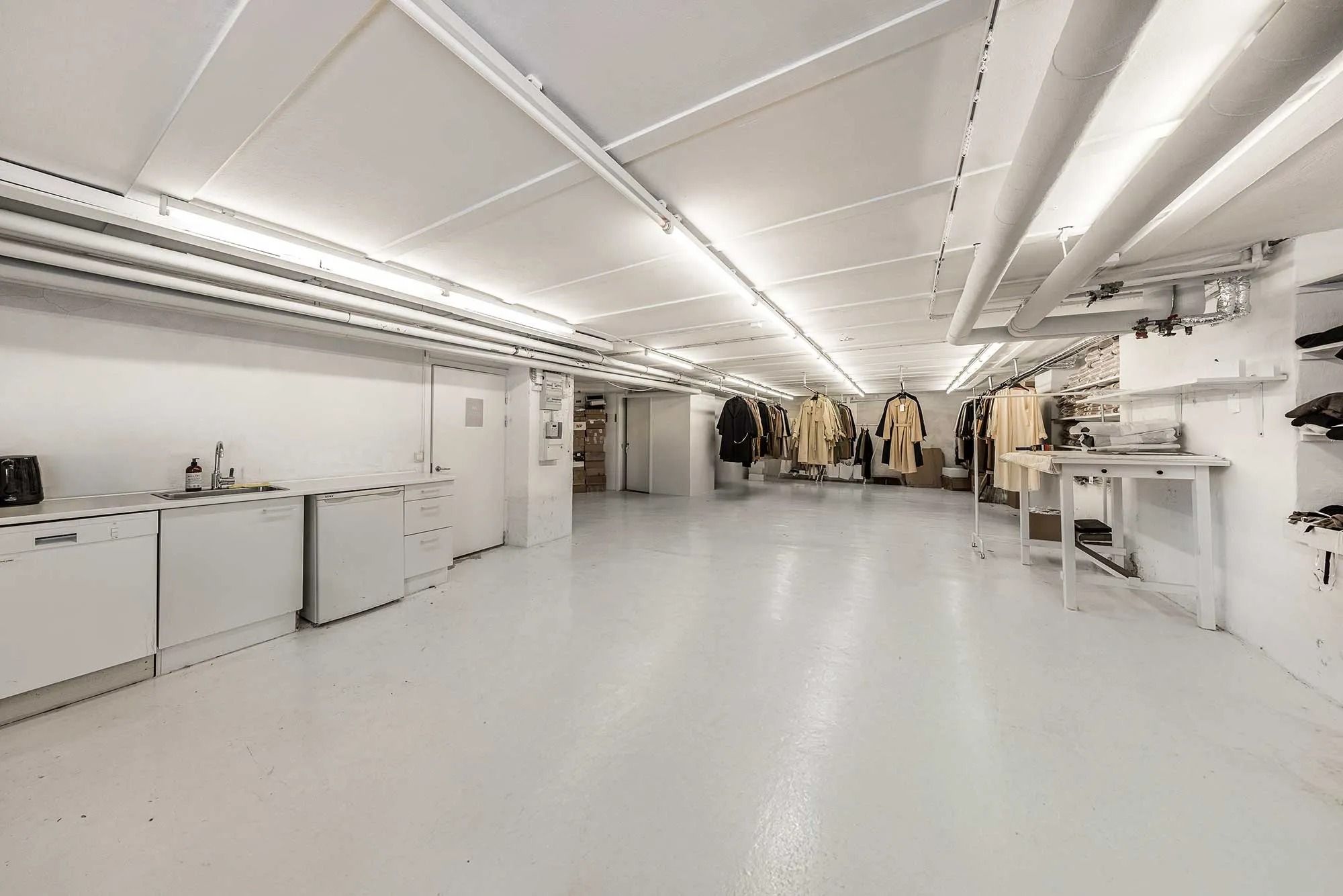 En stor hvid malet lagerrum med en køkkendel, et hængebord og flere hængeklæder