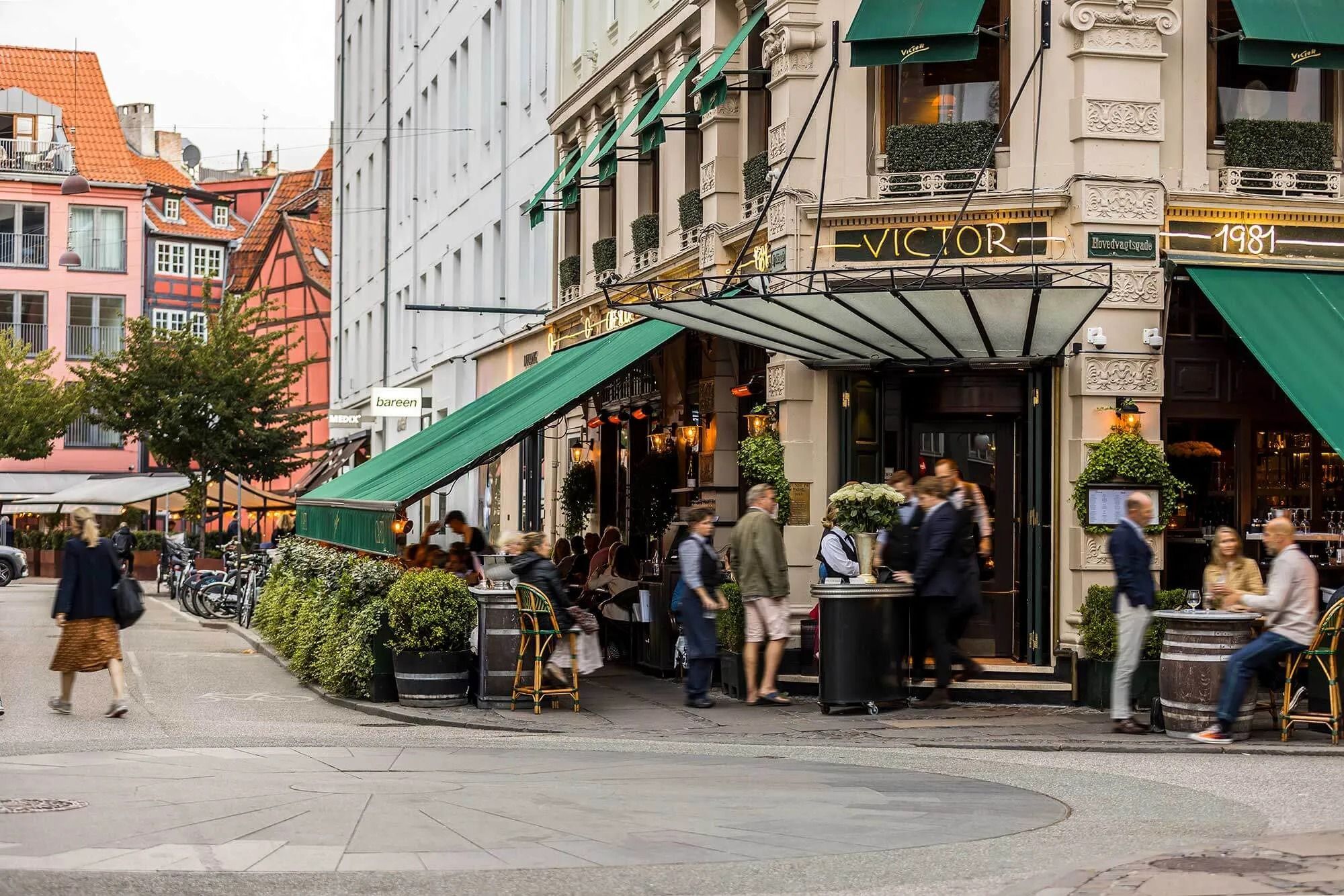 Stilfuld butik med grønne vægge og lysekroner på gågaden i København med mennesker og cykler