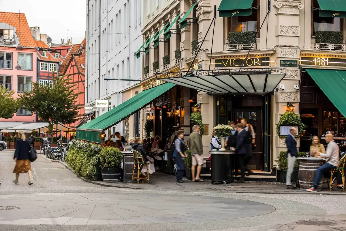 Stilfuld butik med grønne vægge og lysekroner på gågaden i København med mennesker og cykler