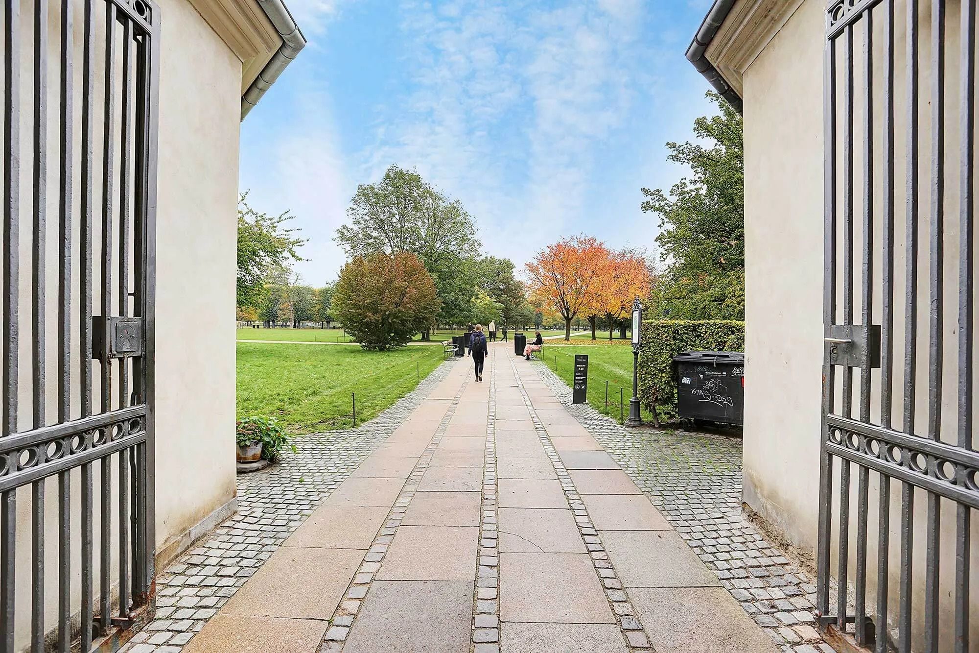 Allerede åbne smedede porten til parken med grønne græsflader og træer med gult og orange løv