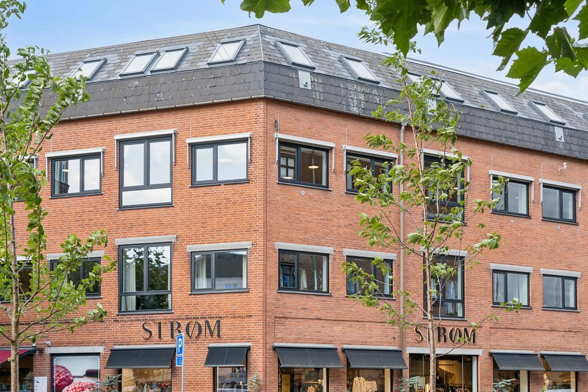 Et lejlighedsbyggeri i tre etager med sort tag og store vinduer, som vender ud mod Strandvejen i Hellerup