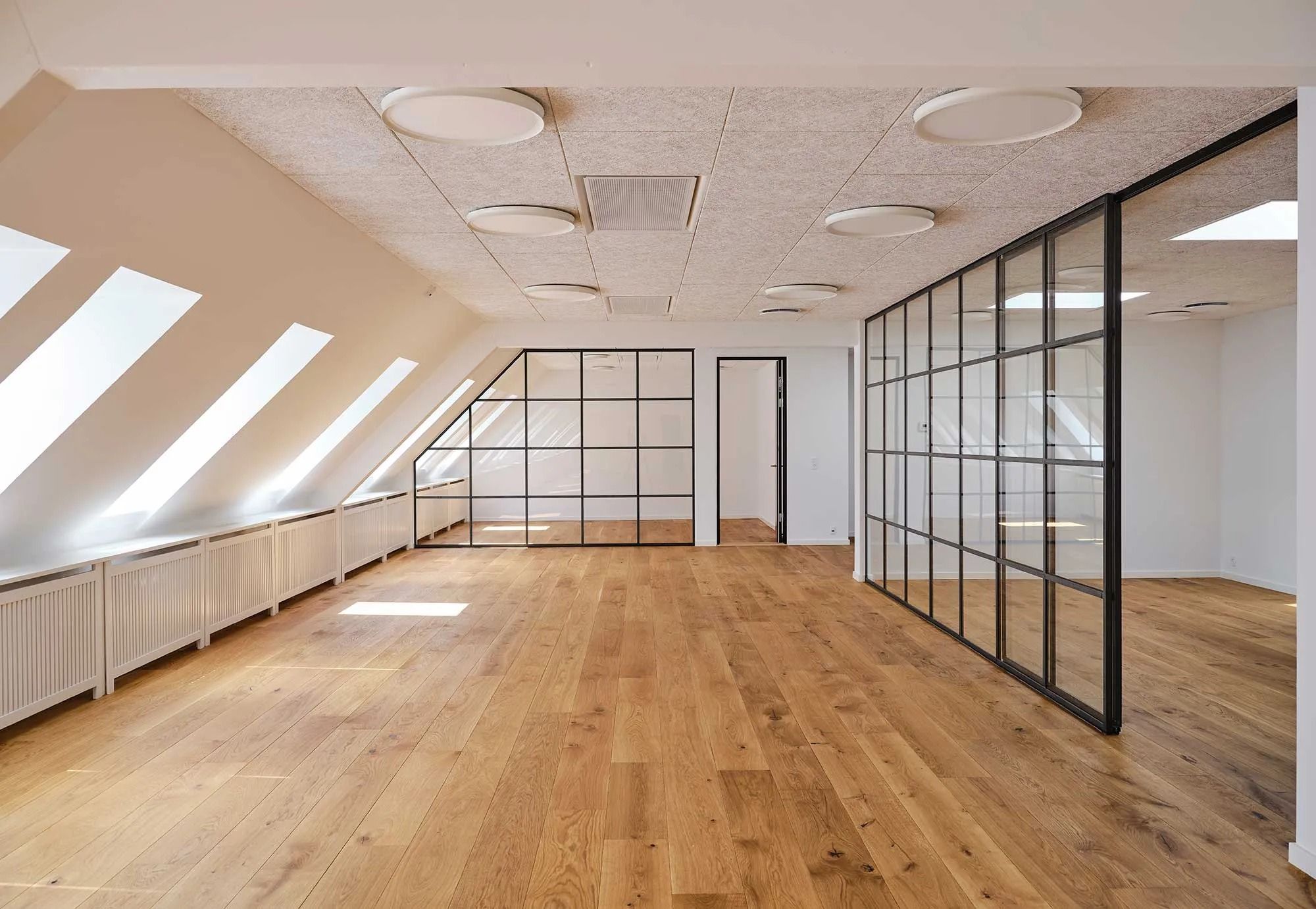 Kontor med lyse lofter, store ruder og lysegule gulvbelægning. Loftet er udstyret med lys og ventilering. Der er flere