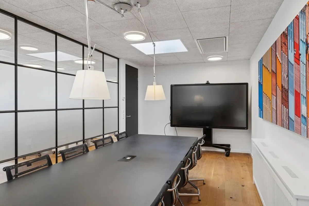 Kontorrum med glasvægge, højloft, projektor, mødesal med lænestol og skrivebord. Lyse loftslampe og moderne interiørdesign.