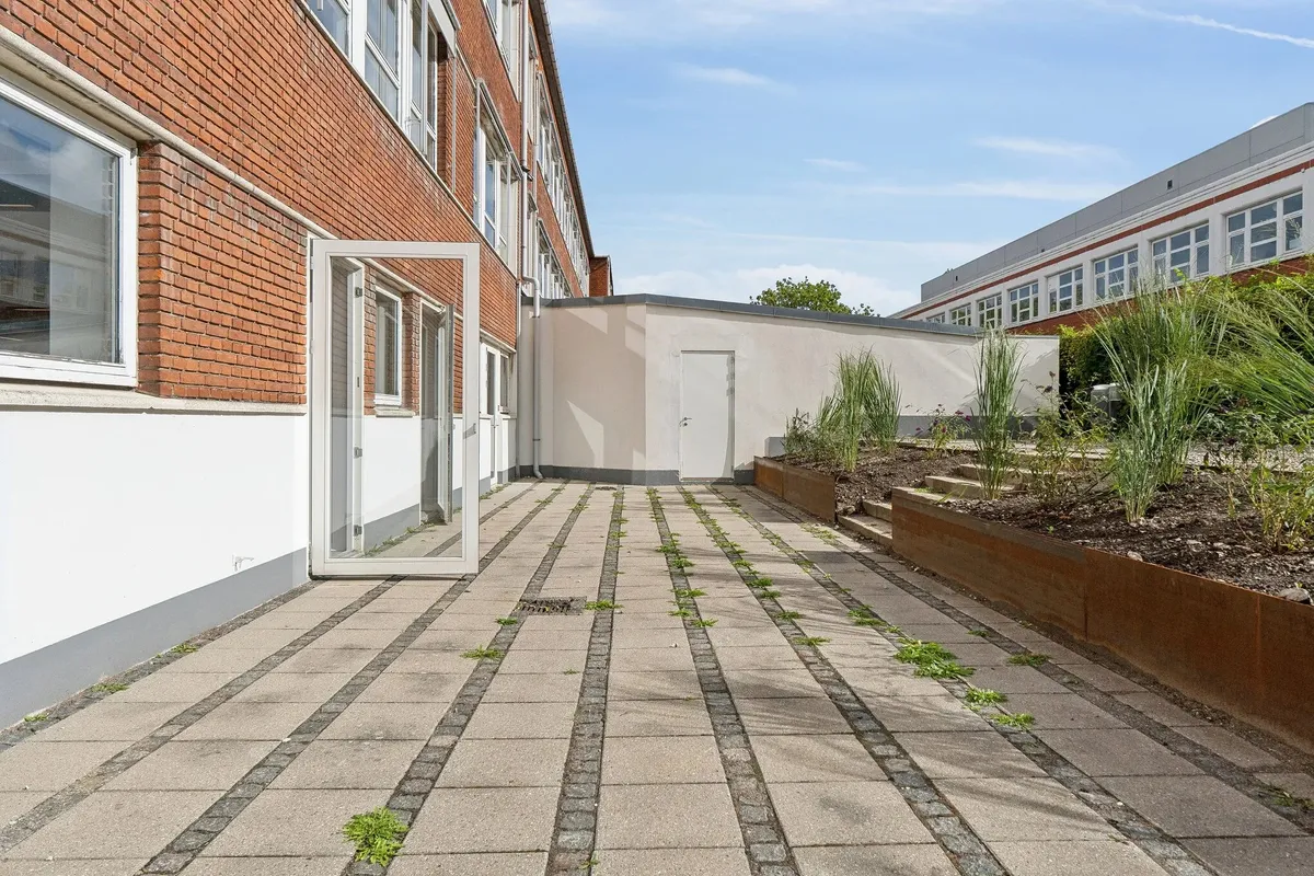 Korte gange og terrasser foran røde murstensbygninger med store vinduer i en lille bydel