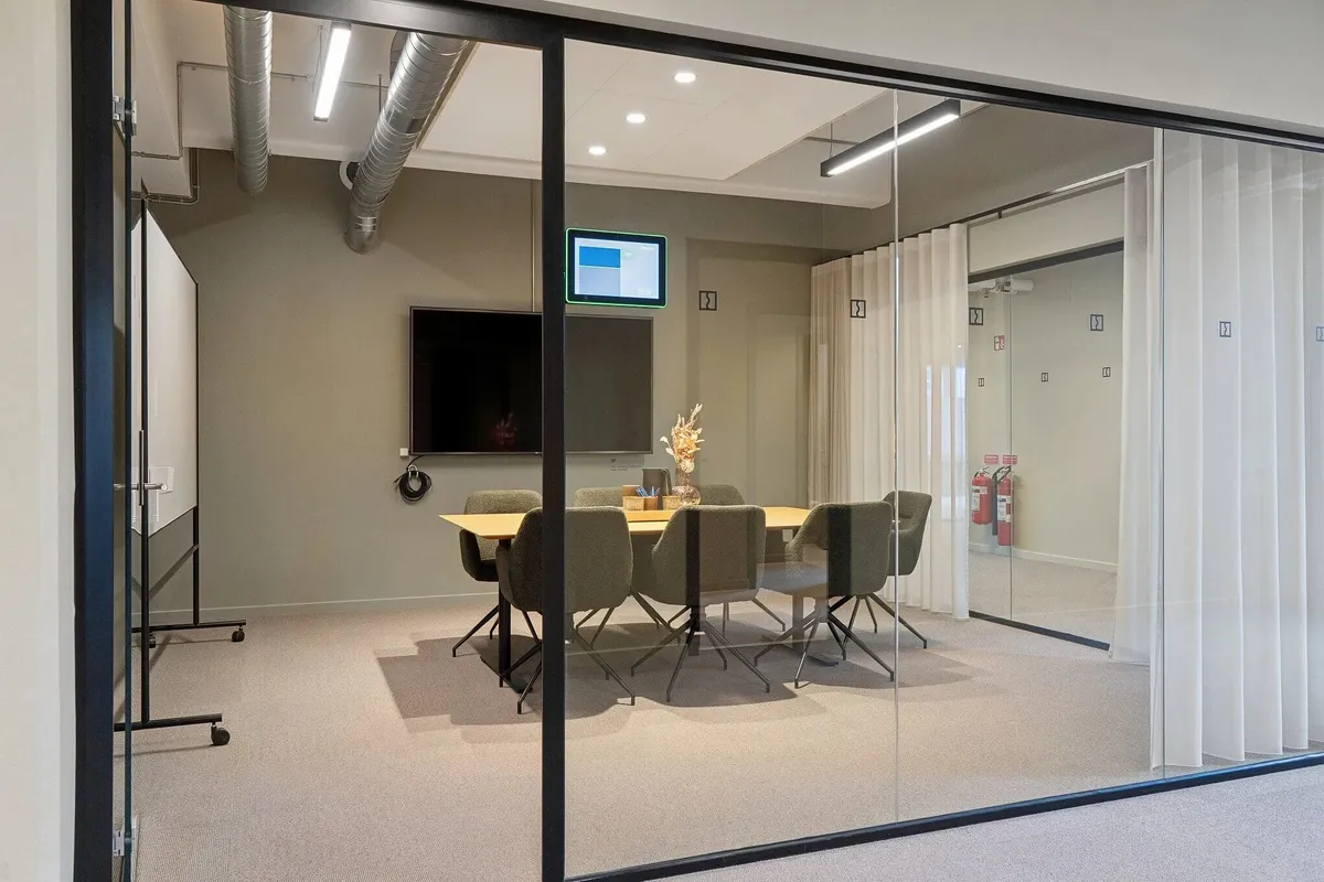 Mødelokrum med moderne møbler og teknologi, herunder en tv-skærm og en skrivebord med blomster og glasflaske